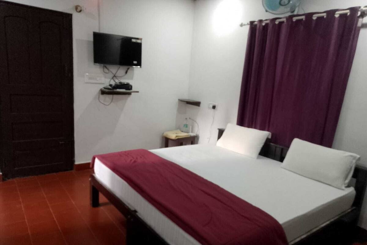A single-bed room with a TV mounted on the wall, a bedside table, and a curtain.