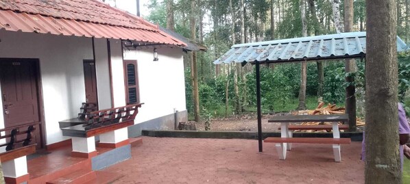 Un edificio rústico con techo rojo, un porche con bancos de madera y una zona de estar al aire libre cubierta.