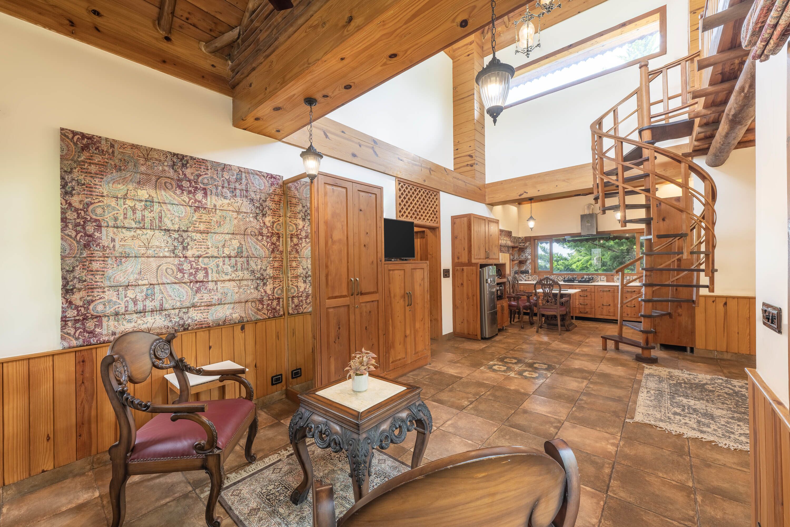 A spacious room with a wooden staircase, a large tapestry, and a dining area.