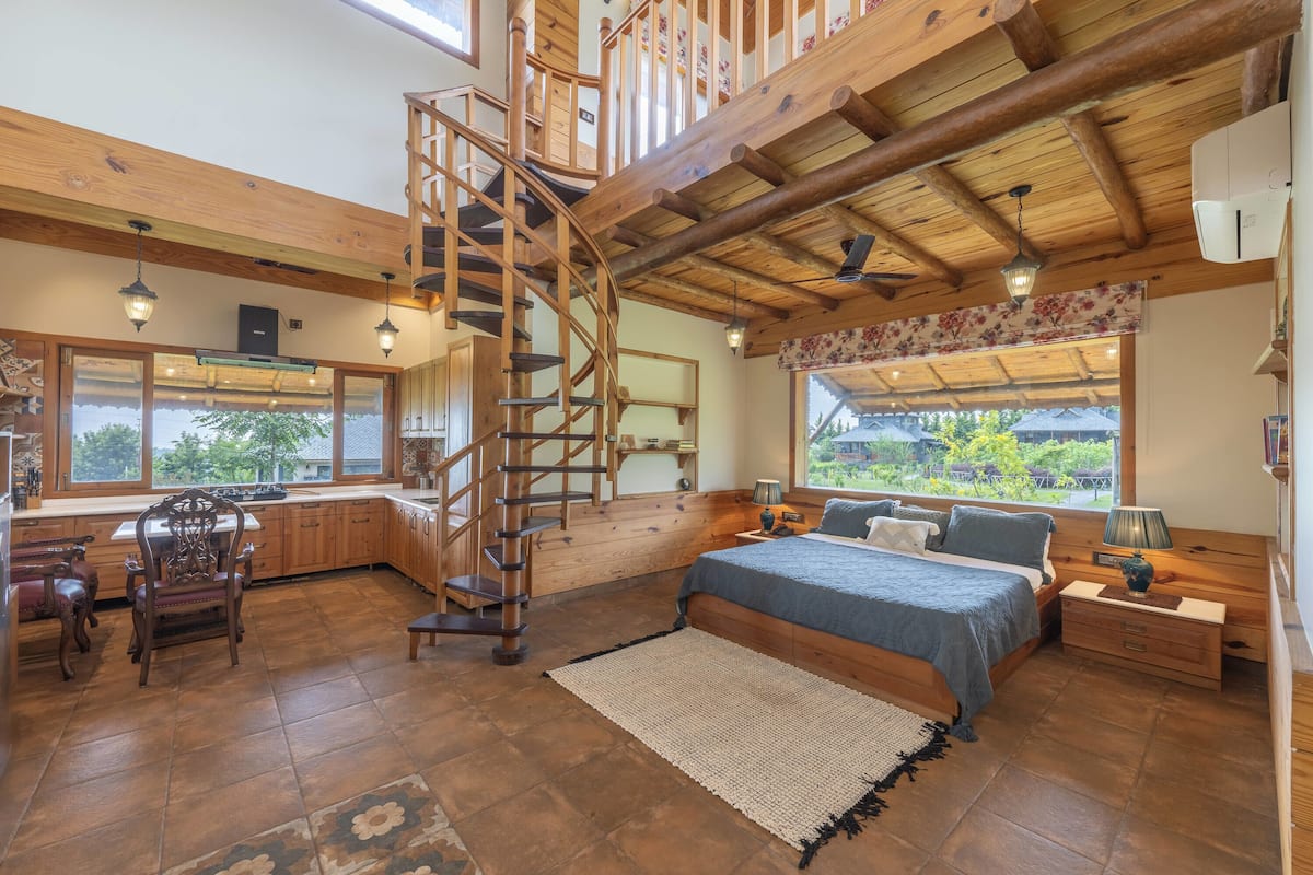 Un dormitorio con una cama grande, una escalera de madera y vistas al exterior.