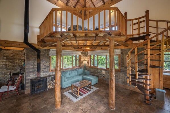 Un vaste espace de vie agrémenté d’un escalier en bois, d’une cheminée et d’une grande fenêtre donnant sur un paysage verdoyant.