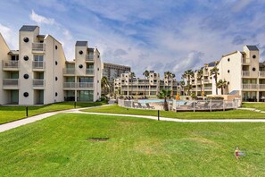 A modern hotel with multiple floors, balconies, and a central pool area surrounded by palm trees.