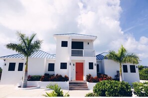 Une maison moderne à deux étages, avec une porte rouge, une façade blanche et un balcon.
