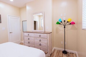 A bedroom with a bed, a dresser, a mirror, and a floor lamp. - Tropical Apartment Near Long Bay with Pool Access (Leeward Settlement)