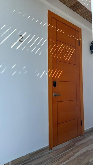 A wooden door with a keypad lock, a small window, and a wall-mounted light fixture.