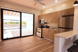 A modern kitchen with wooden cabinets, stainless steel appliances, and a large sliding glass door leading to a balcony. - Tropical Apartment Near Long Bay with Pool Access (Leeward Settlement)