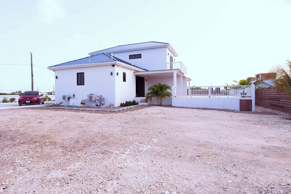A two-story white house with a blue roof, a balcony, and a gravel driveway.