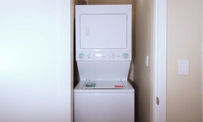 A compact, white, stacked washer and dryer unit in a narrow hallway.