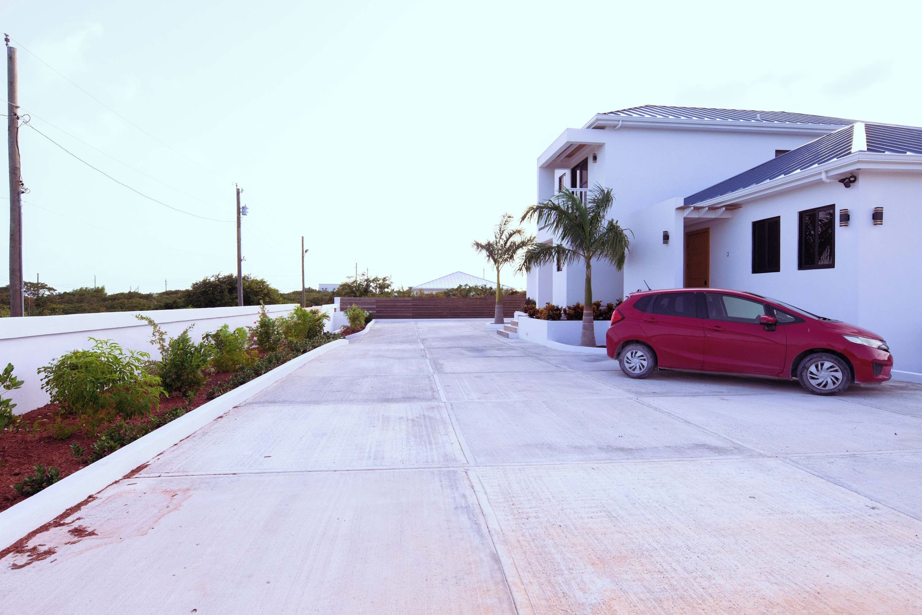 Una casa moderna con un coche rojo aparcado en la entrada, rodeada de un jardín cuidado y un cielo despejado.