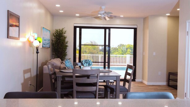 A dining area with a table and chairs, a ceiling fan, and a view of a balcony with a pool. - Private Pool Villa Near Long Bay Beach & Grace Bay (Leeward Settlement)