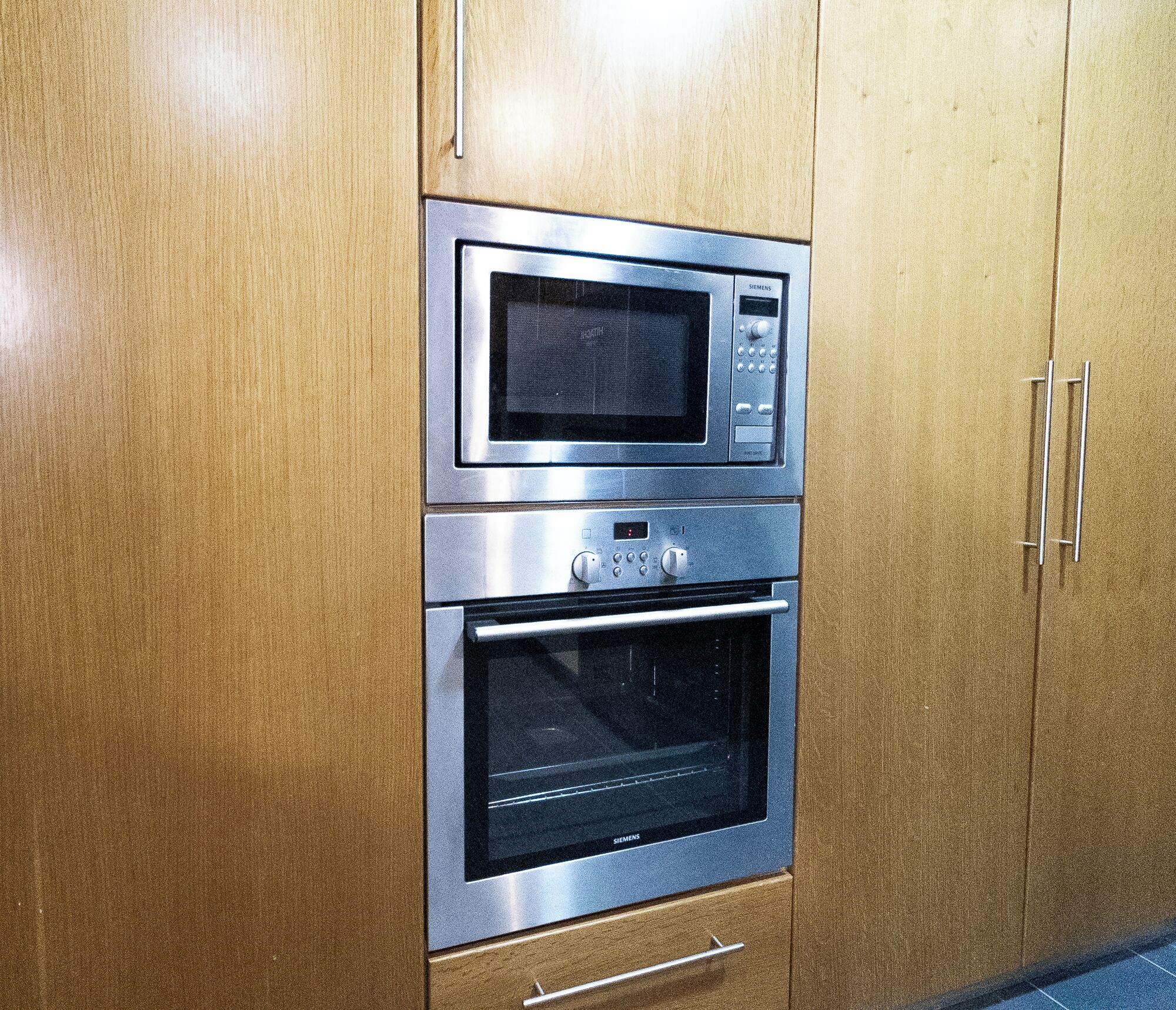 A kitchen with a built-in microwave and oven, wooden cabinets, and stainless steel appliances.