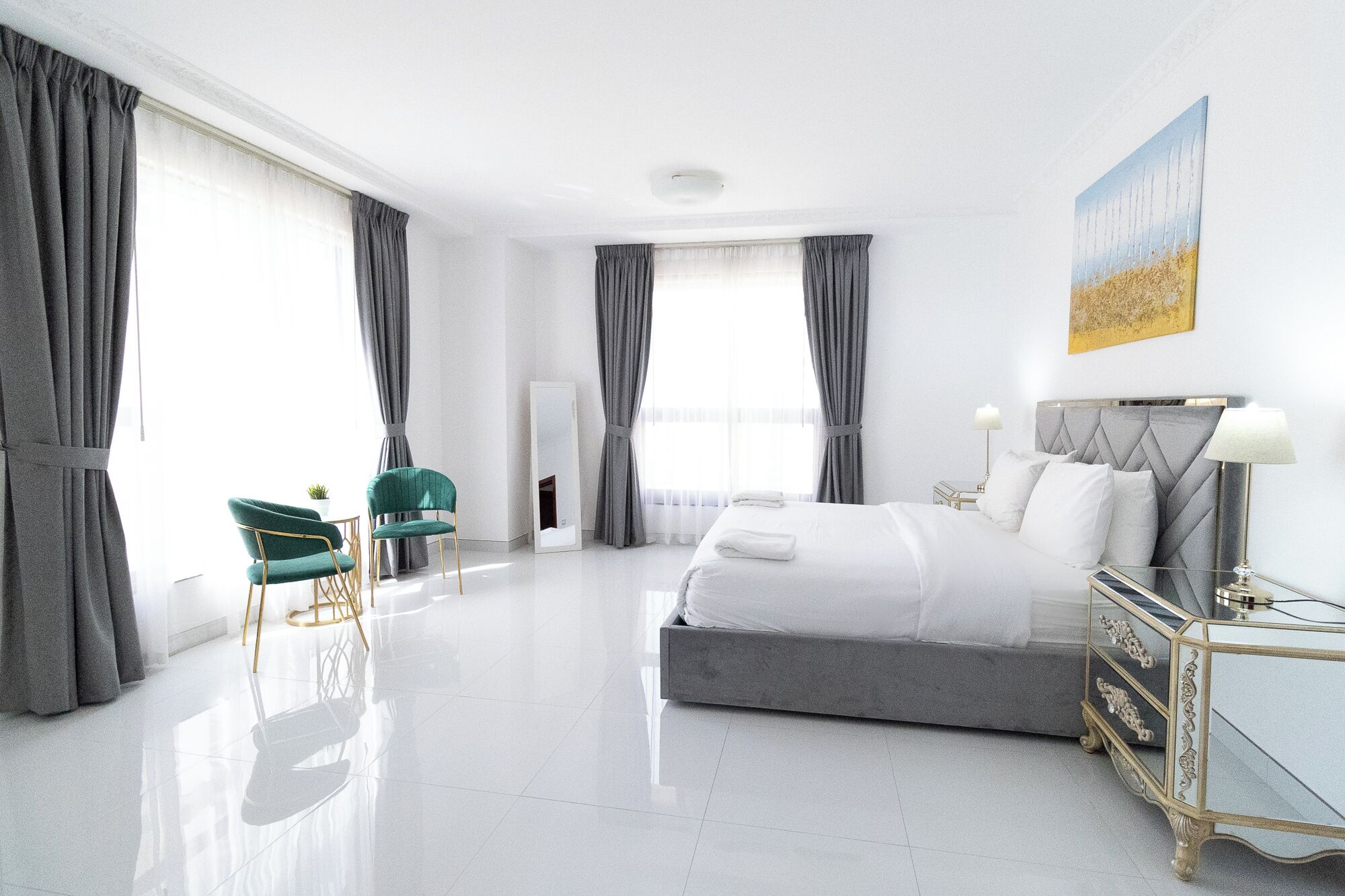 Habitació d'hotel moderna amb un llit gran, una zona de seients amb una cadira, una taula de nit i un mirall.