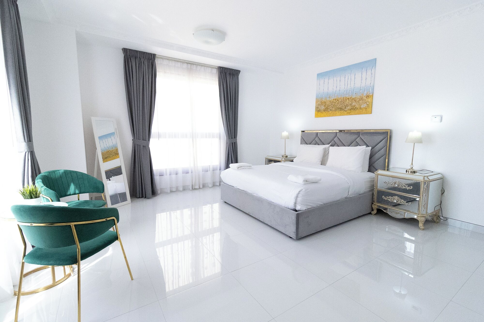 A modern hotel room with a large bed, a green upholstered chair, a bedside table with a lamp, and a painting on the wall.