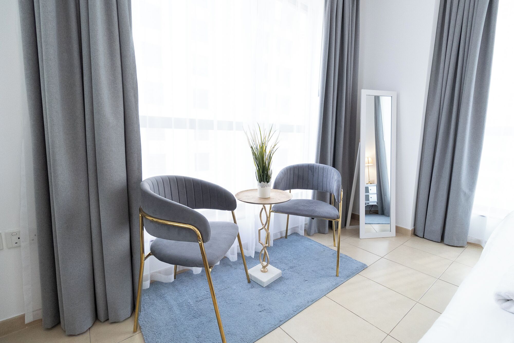 Ein modernes Wohnzimmer mit grauen Polstersesseln, einem runden Tisch und einem blauen Teppich.