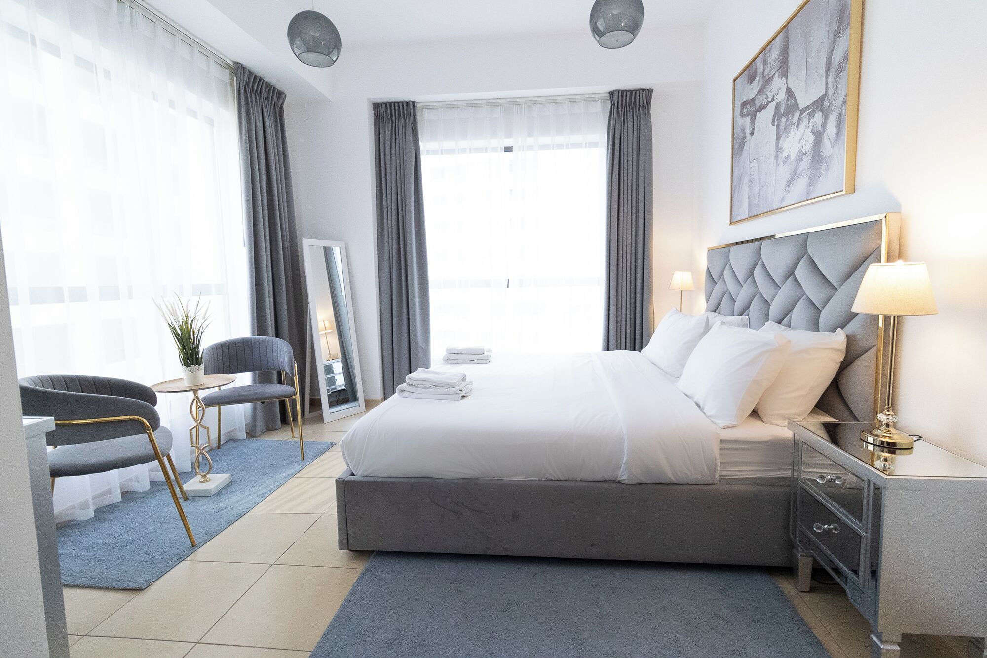 Ein modernes Hotelzimmer mit einem großen Bett, einem Nachttisch mit Lampe, einem Sessel, einem Schreibtisch und einem großen Fenster mit Vorhängen.