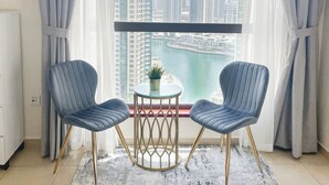 A modern room with two blue chairs, a small round table with a plant, and a view of a cityscape through large windows. - HAPPY SEASON | Apartment on JBR  (Dubai)