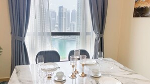 A dining table set with plates, glasses, and cutlery, with a view of a cityscape through a window. - HAPPY SEASON | Apartment on JBR  (Dubai)