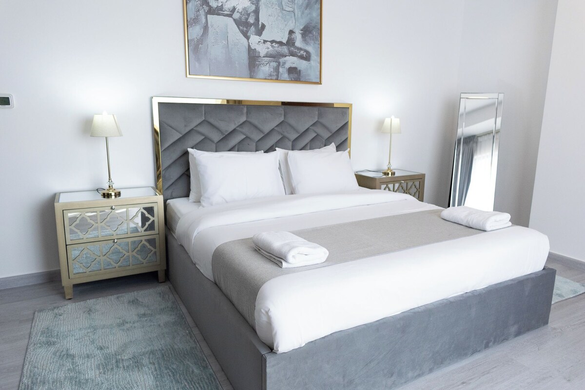 A modern hotel room with a large bed, two bedside tables, a headboard, and a large mirror.