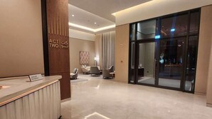 Un hall d’accueil moderne, doté d’un comptoir de réception, d’une grande porte vitrée donnant sur le hall, et d’un espace intérieur spacieux avec un plafond haut et un éclairage encastré.