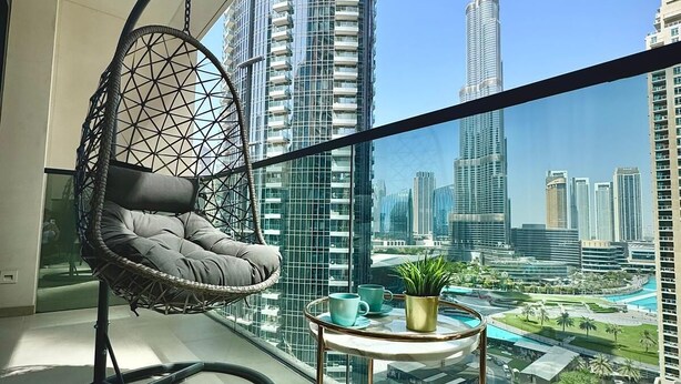 Un balcon avec un fauteuil suspendu, une petite table agrémentée d’une plante, et une vue sur le Burj Khalifa.