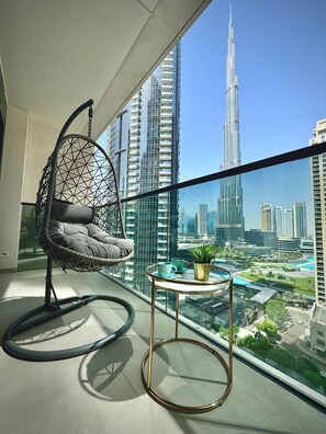 A balcony with a hanging chair, a small table with a plant, and a view of the Burj Khalifa.