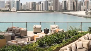 A rooftop terrace with outdoor seating, a view of a city skyline, and a body of water. - HAPPY SEASON | Four Season apartment  (Abu Dhabi)