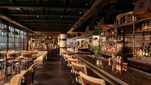 A bar with high stools and a long counter, large windows, and a view of the city. - HAPPY SEASON | Four Season apartment  (Abu Dhabi)