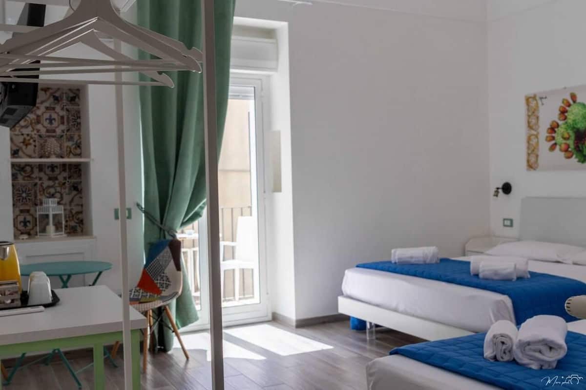 A hotel room with a bed, a table with a chair, a hanging rack, and a view of the outside.