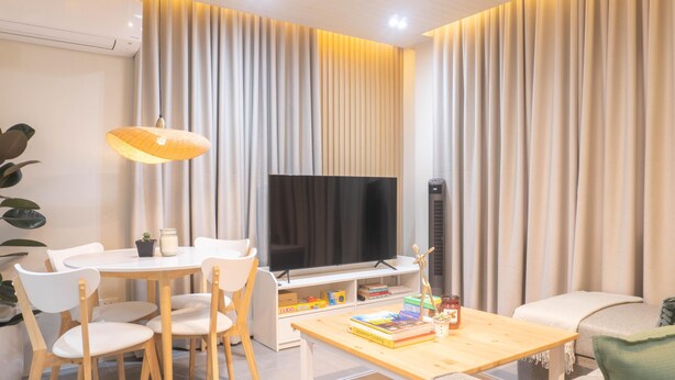 A modern living room with a flat-screen TV, a dining table with chairs, a bookshelf, and a large window with curtains. - Charming 2-bedroom villa in gorgeous Tagaytay with AC, WiFi (Tagaytay)