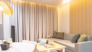 A modern living room with a grey sofa, a small table with books, a potted plant, and a standing heater. - Charming 2-bedroom villa in gorgeous Tagaytay with AC, WiFi (Tagaytay)