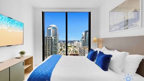 Ein modernes Hotelzimmer mit einem großen Bett, Blick auf die Stadt, einem Fernseher und einem Holztisch.