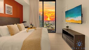 A modern hotel room with a large bed, a TV, and a city view.