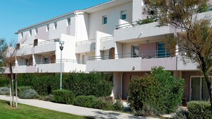 A multi-story hotel with balconies, a paved walkway, and well-maintained landscaping. - Cap Med by Interhome (Le Grau du Roi)