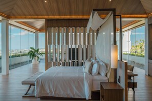 A modern bedroom with a large bed, a bedside table, a lamp, and a view of the city. - Beyond The Sea (Jimbaran)