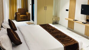 A hotel room with a bed, a chair, a wardrobe, a desk, and a television.