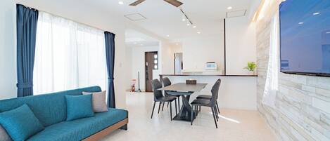 A modern living room with a sofa, dining table, chairs, and a ceiling fan.