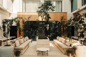 Un patio interior moderno con un área de estar central, rodeado de mesas y macetas.