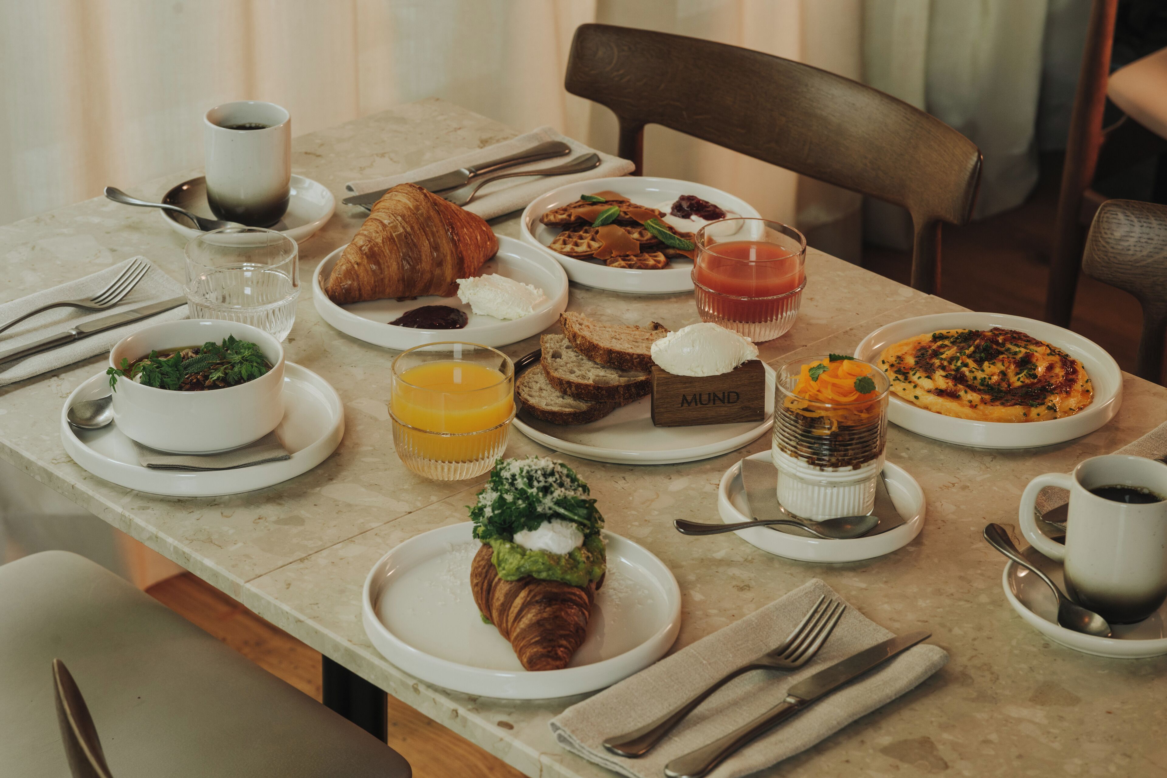A breakfast table with various dishes, including croissants, toast, and a fruit bowl.