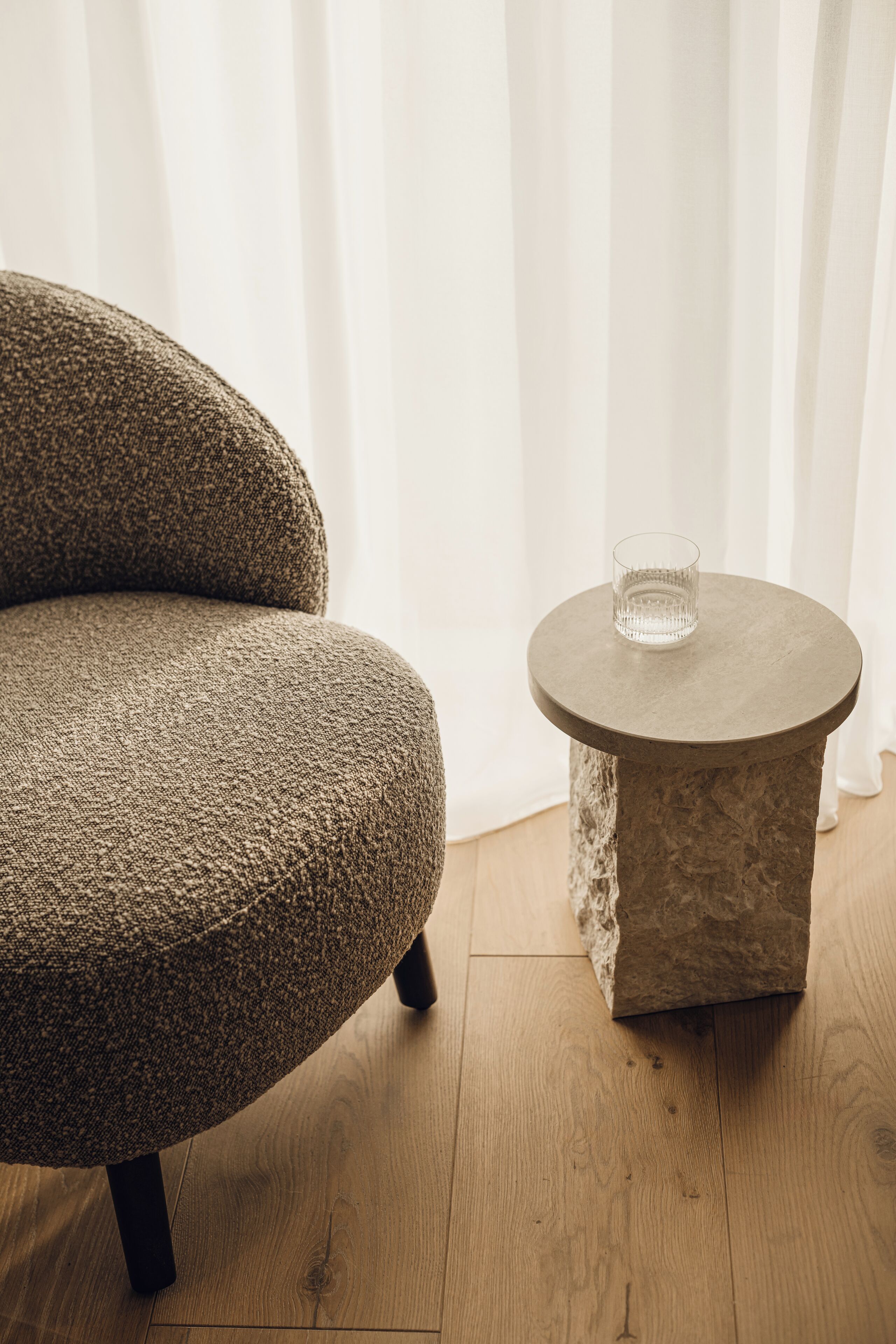 Une pièce avec un fauteuil à l’assise texturée et une table ronde sur laquelle se trouve un verre.