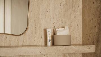 Une salle de bain avec un mur en marbre, un miroir et une étagère où sont rangés les articles de toilette.