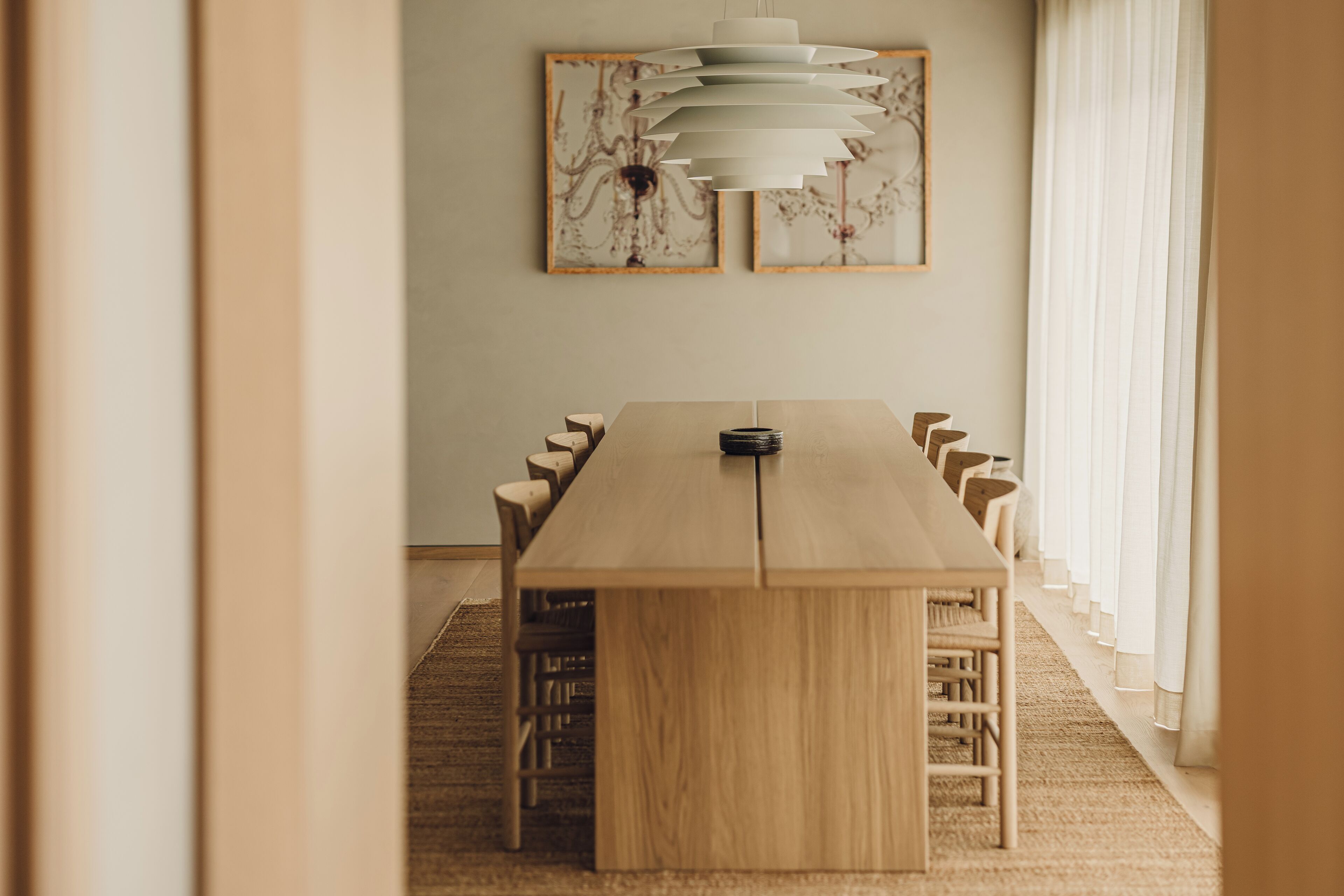Una larga mesa de conferencias de madera con sillas alrededor, ubicada en una habitación con un ventanal y cortinas.