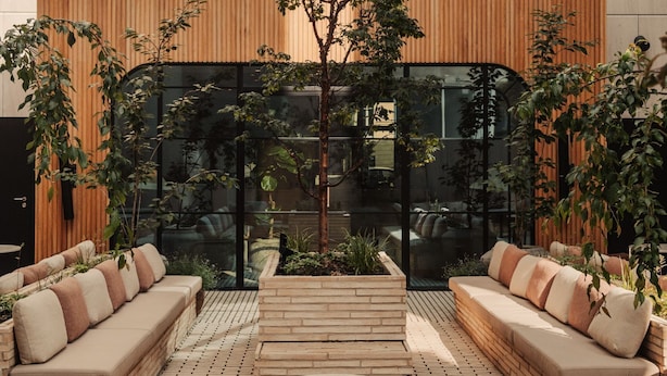 Un espace de détente extérieur moderne, composé de deux canapés et d’une petite table, entouré de plantes et d’un mur en bois.