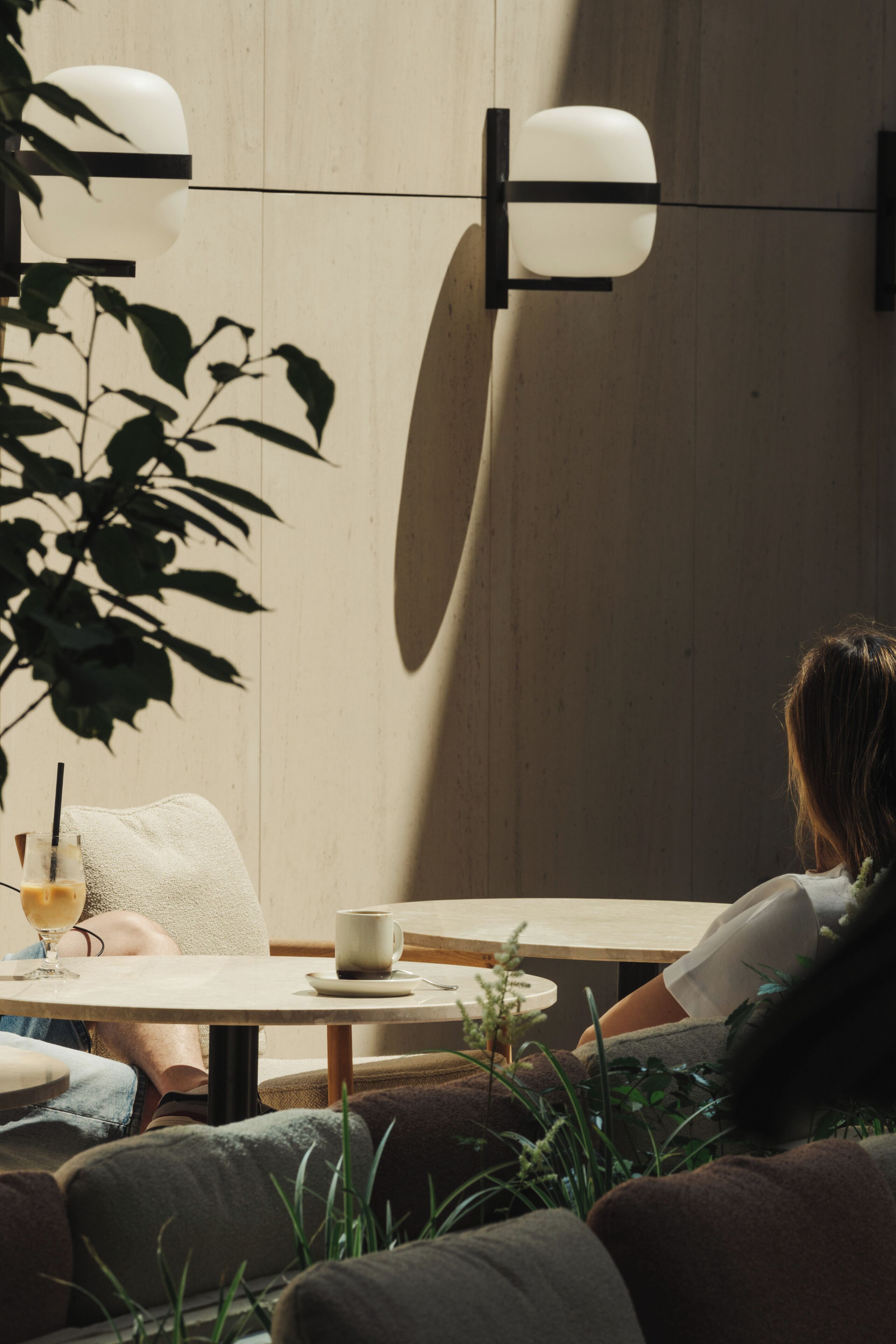 Une personne assise à une table ronde, devant laquelle se trouvent une plante, un verre et une tasse.