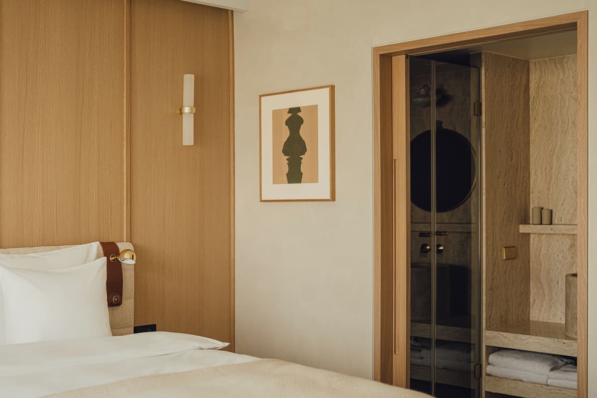 Ein Hotelzimmer mit einem großen Bett, einem Holzschrank, einem gerahmten Kunstwerk an der Wand und einem durch eine offene Tür einsehbaren Badezimmer.