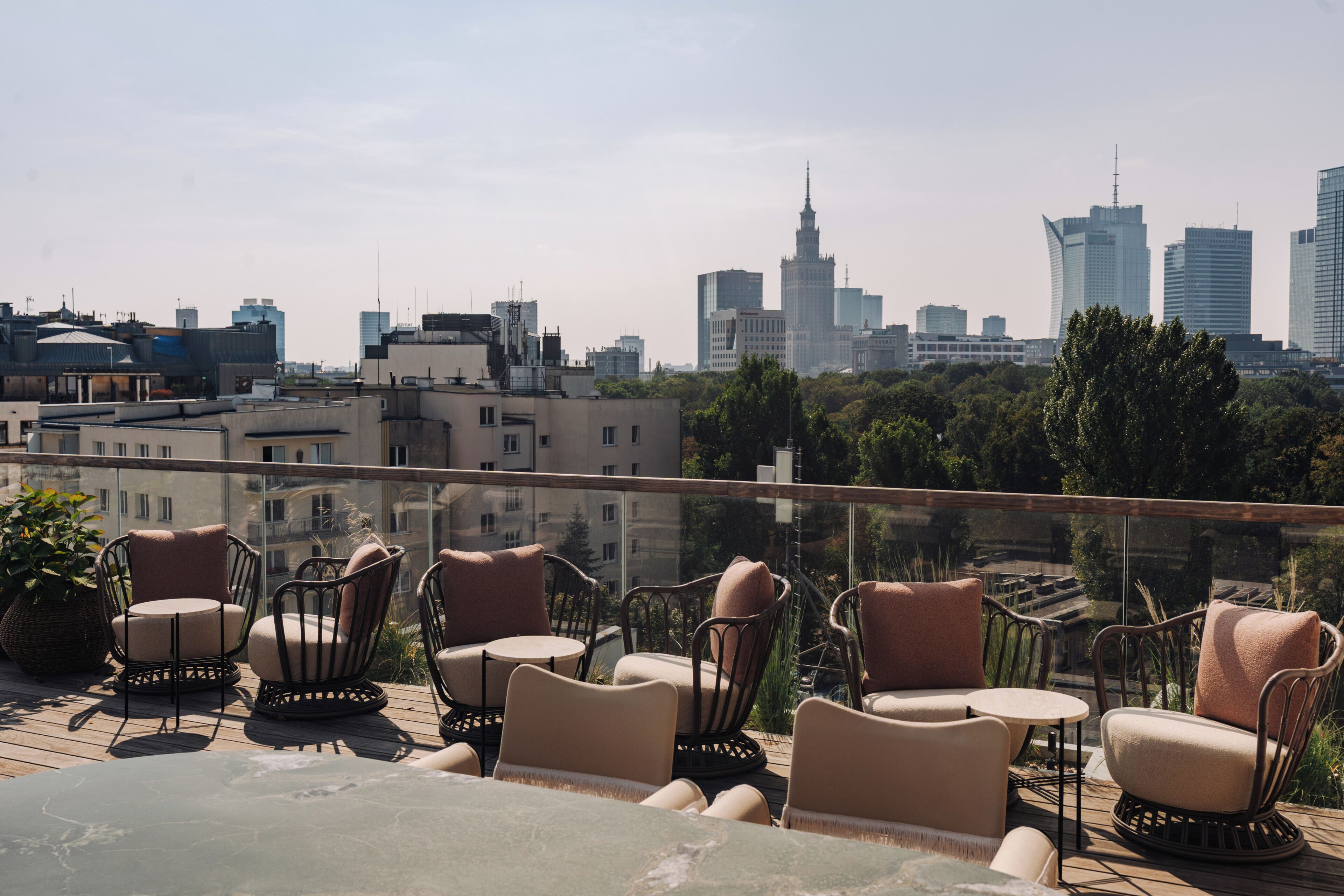 Terraza en la azotea con sillas de mimbre y una mesa, con vistas a un paisaje urbano con edificios modernos.