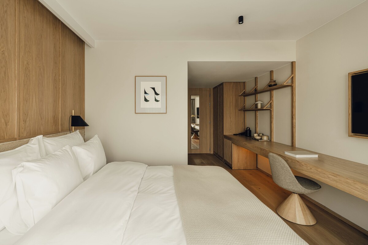 Una habitación de hotel con una cama, un escritorio, una silla, un cuadro enmarcado y un armario de madera.