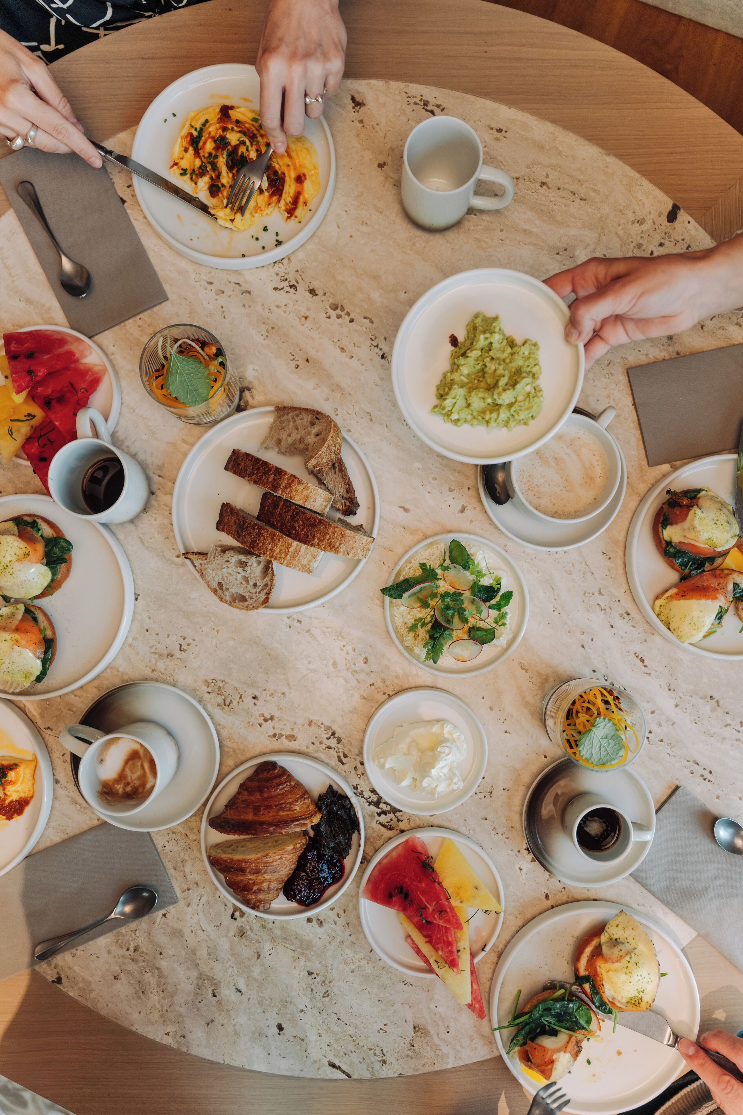 Een ronde tafel met diverse gerechten en drankjes, zoals brood, salades en koffie.