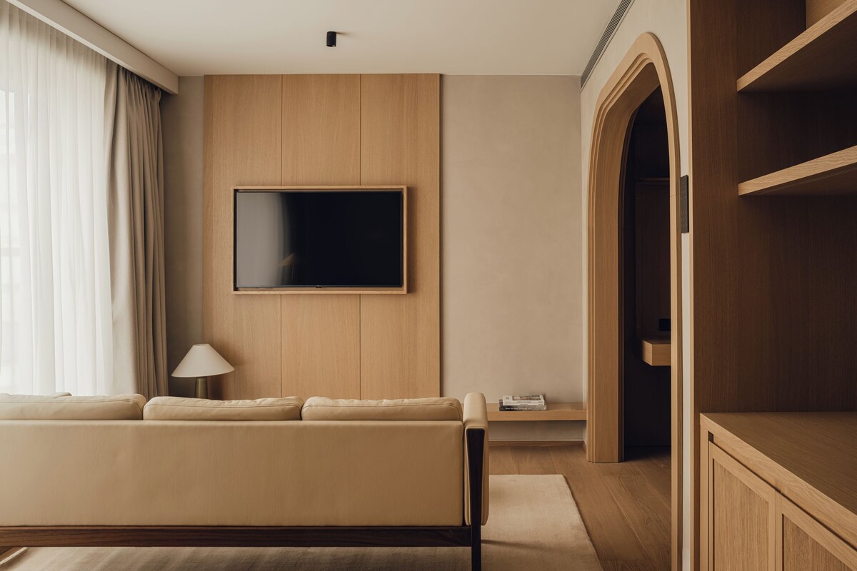 Een moderne woonkamer met een bank, een flatscreen televisie aan de muur, houten vloeren en een inbouwmeubel.