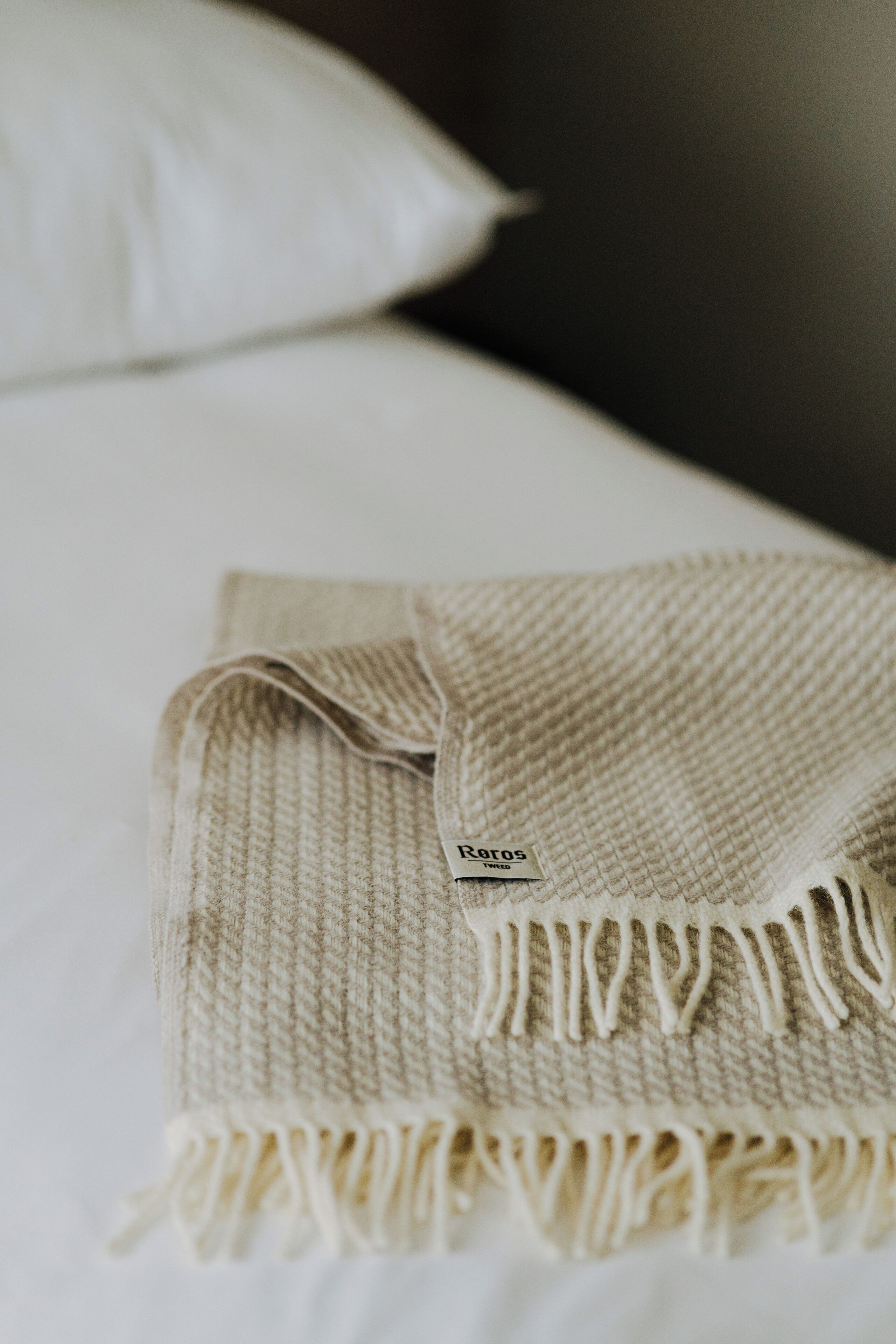 Una manta beige doblada con flecos sobre una cama.