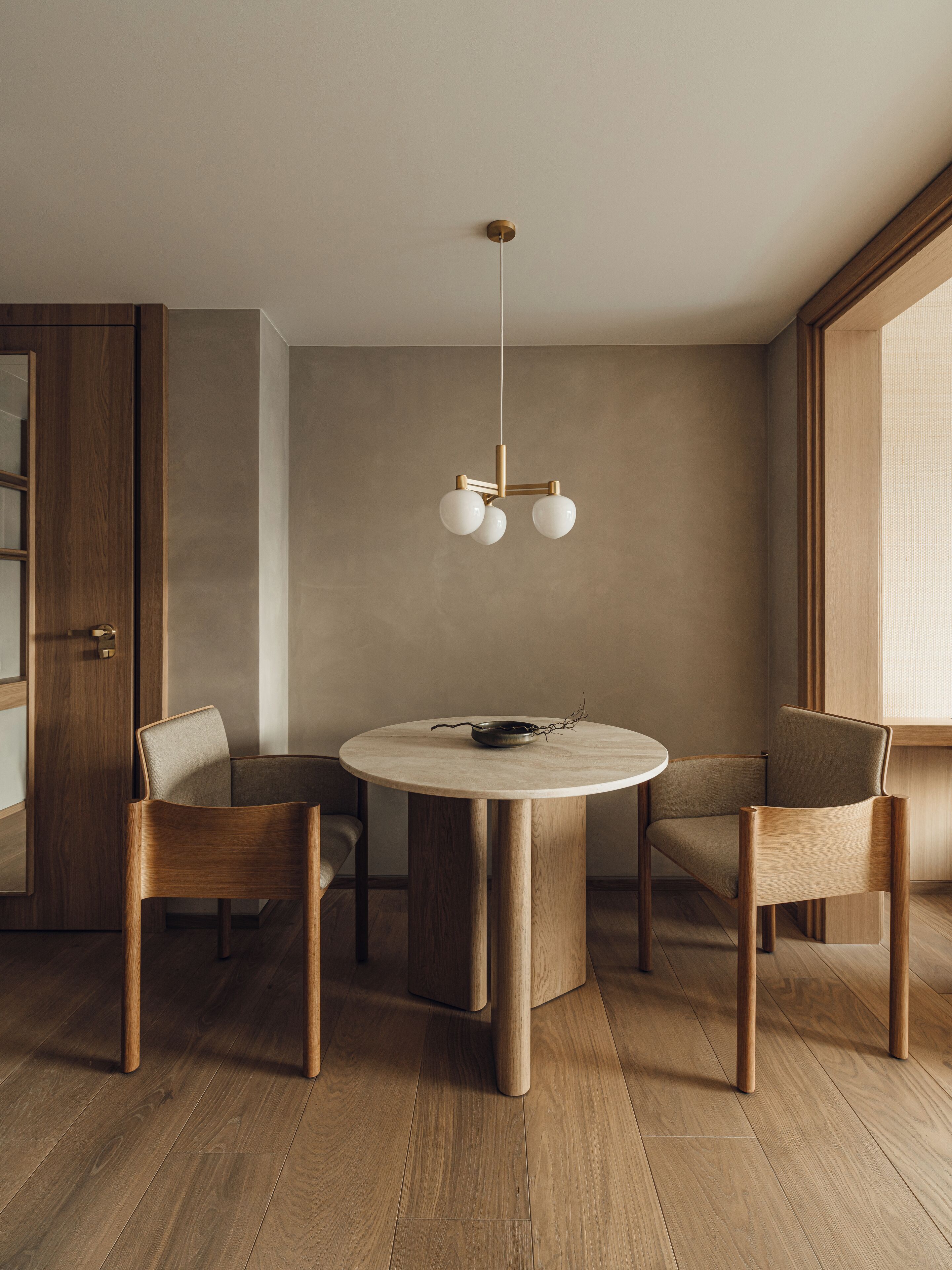 A modern dining area with a round table, two wooden chairs, and a minimalist pendant light.